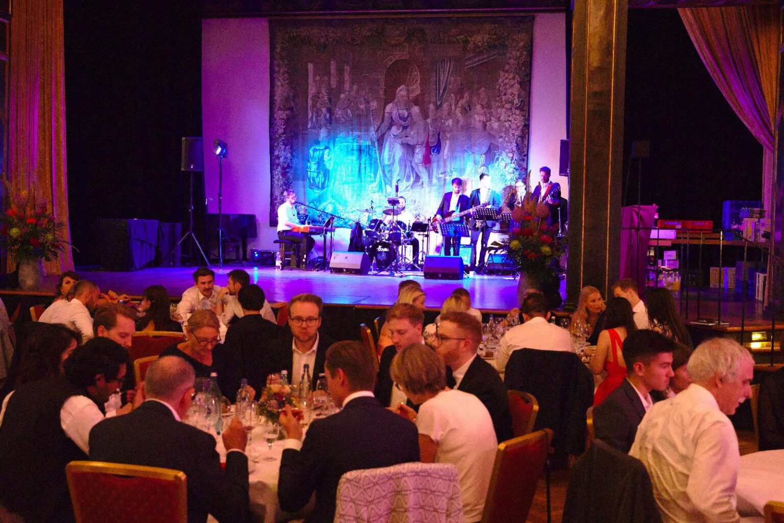 Die Brass Tacks Band spielt stilvolle, zurückhaltende Dinner-Musik auf einem Gala-Event, elegant gekleidet und dezent beleuchtet.