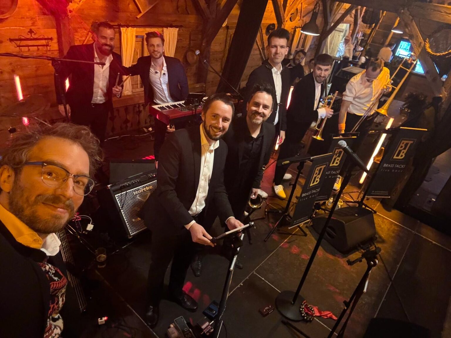 Die Brass Tacks Band spielt live auf einer gemütlichen Hüttenparty mit rustikalem Ambiente und gut gelaunten Gästen.