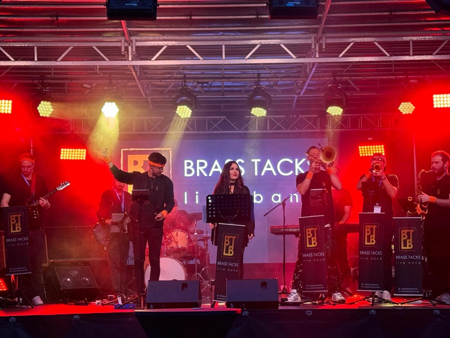 Die Brass Tacks Band spielt auf einer Bühne mit bunten Lichtern und einer beeindruckenden Lichtshow, die Party und Stimmung perfekt untermalen.