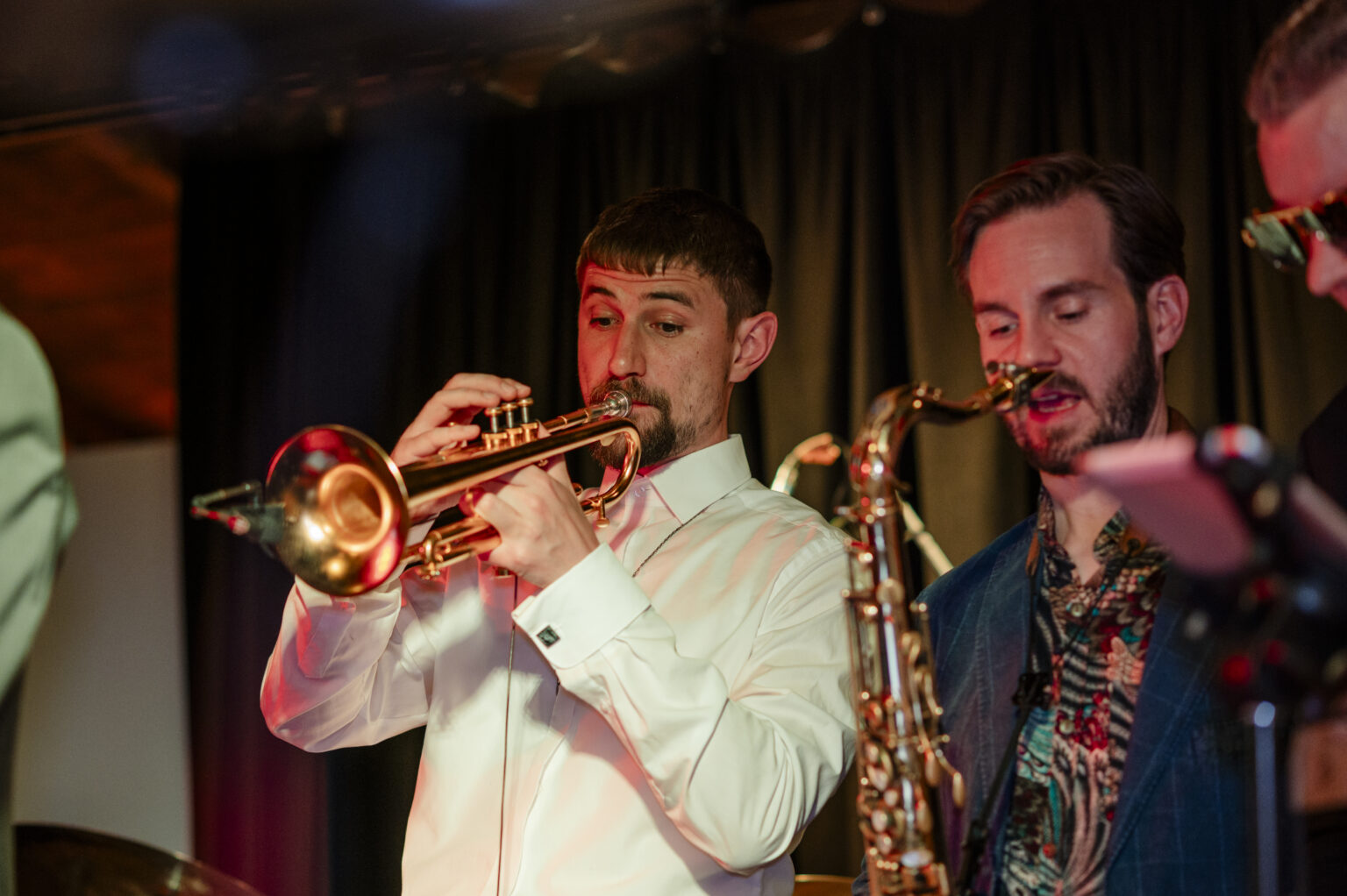 Trompete und Saxophon der Brass Tacks Band stehen im Scheinwerferlicht und bereiten sich darauf vor, kraftvolle, lebendige Melodien zu spielen.