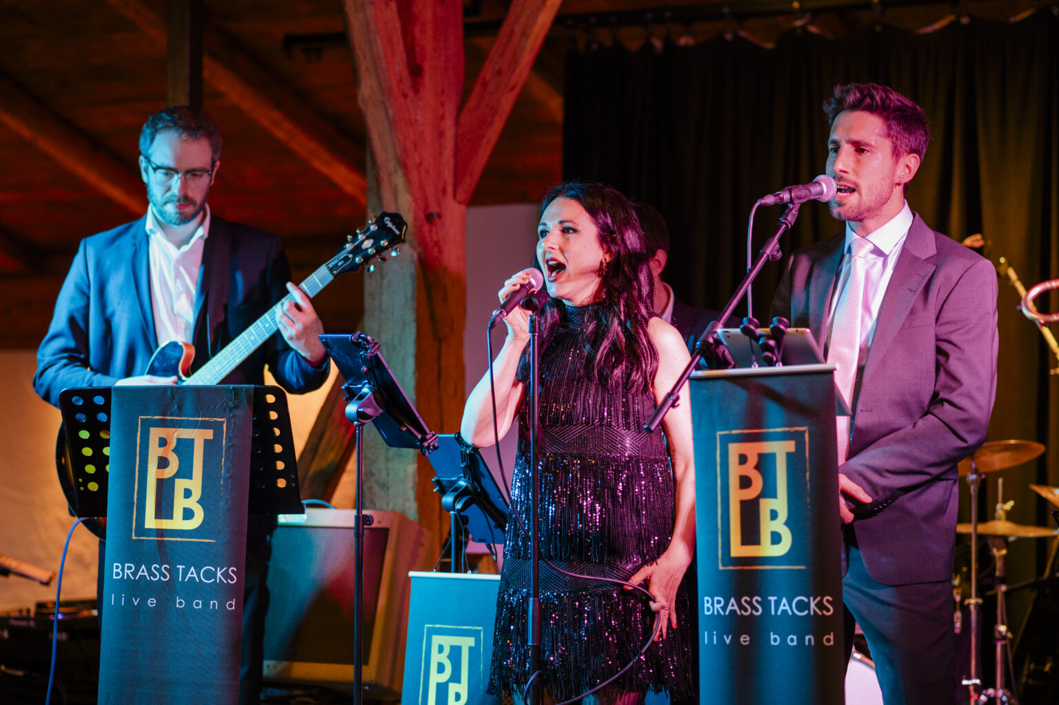 Die beiden Sänger der Brass Tacks Band stehen gemeinsam im Spotlight und singen perfekt aufeinander abgestimmt, mit spürbarer Harmonie und Bühnenchemie.